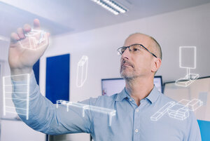 Ein Planer verschiebt symbolhaft vor einer Glaswand Objekte von der realen in die digitale Welt.