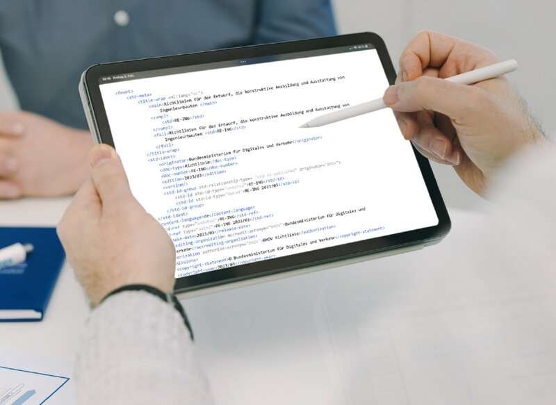Foto: Markus Braumann Eine Hand hält einen Tablet-Computer. Auf dem Bildschirm sind technische Code-Zeilen zu sehen, die die Transformation von Richtlinien in Smarte Standards darstellen.